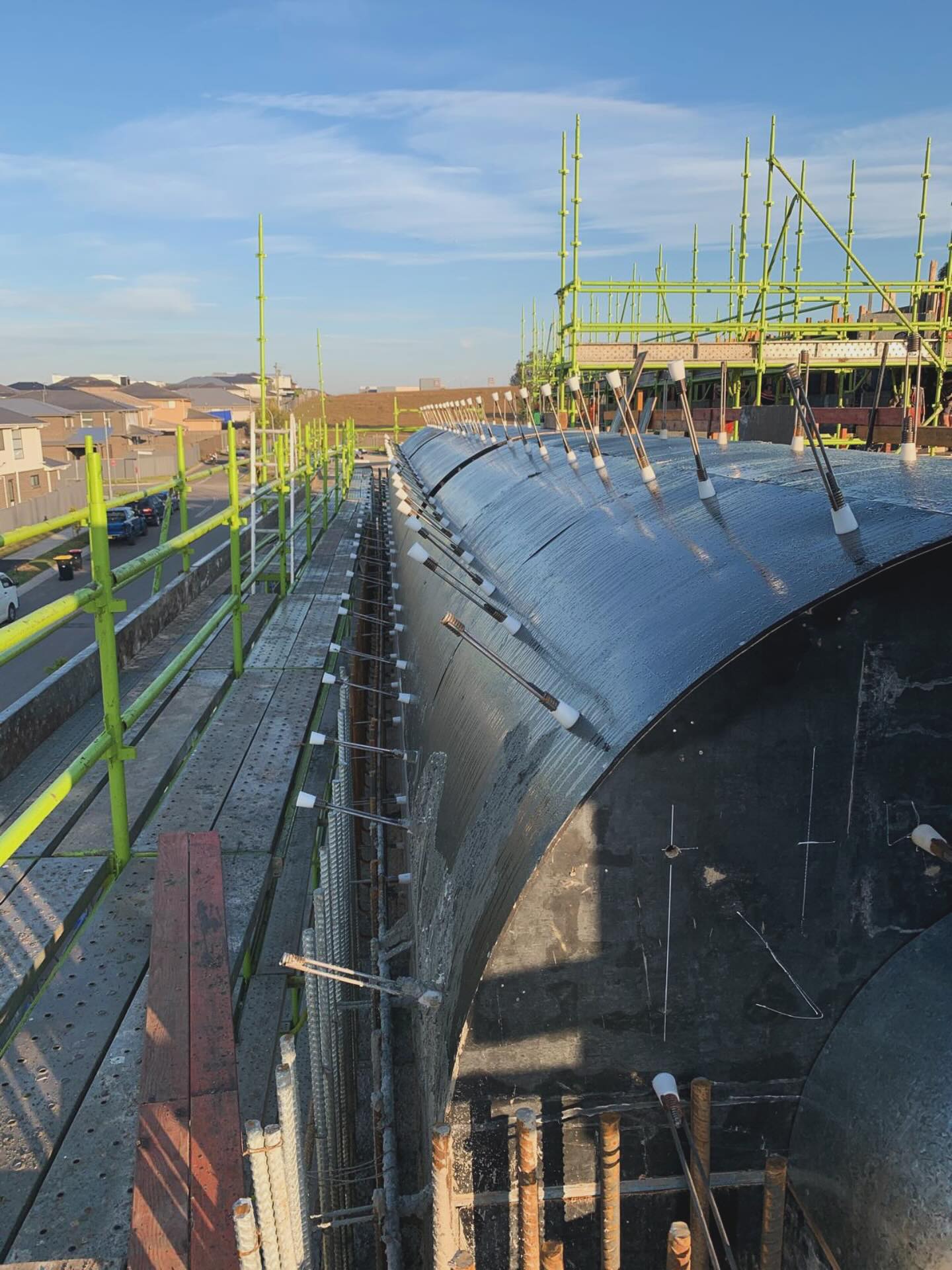 Curved black wall formwork installed beside green scaffold